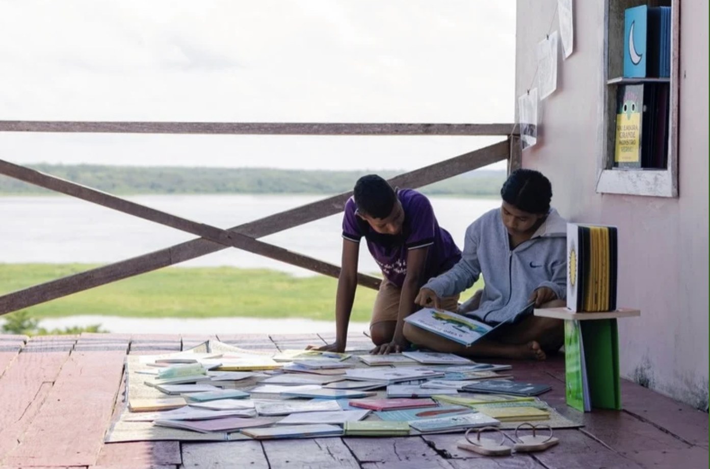 Two young readers laying out books on the deck of the community library in Uarini